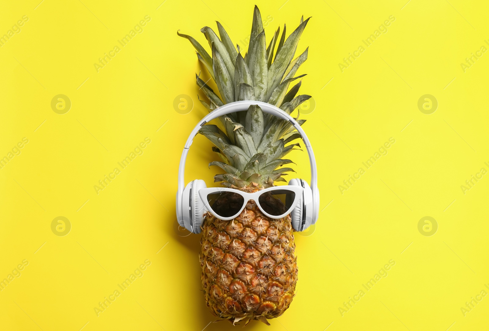 Photo of Pineapple with sunglasses and headphones on yellow background, top view. Creative concept