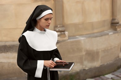 Photo of Young nun with Christian cross and Bible near building outdoors, space for text