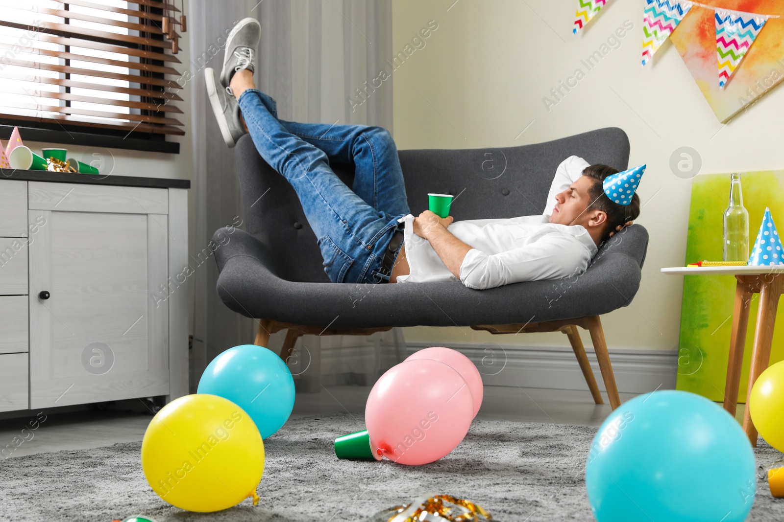 Photo of Man sleeping on sofa in messy room after party