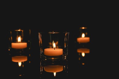 Photo of Burning candles in glass holders on table against dark background