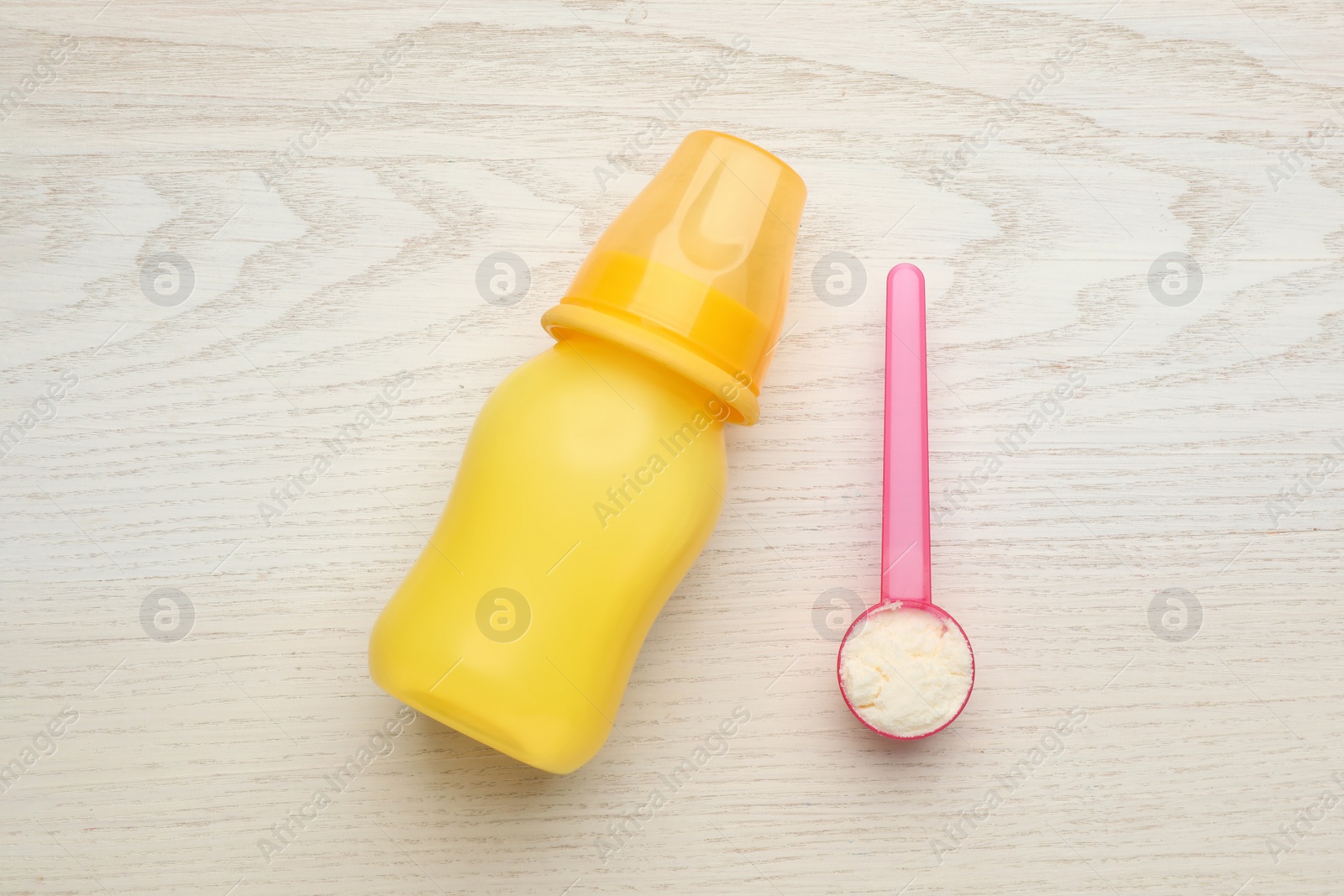 Photo of Feeding bottle with infant formula and powder on white wooden table, flat lay