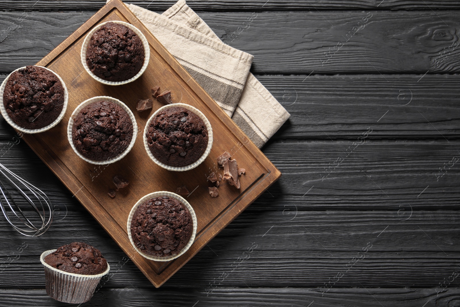 Photo of Delicious chocolate muffins on black wooden table, flat lay. Space for text