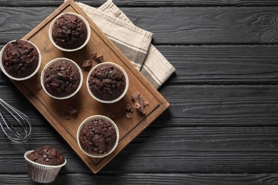 Delicious chocolate muffins on black wooden table, flat lay. Space for text