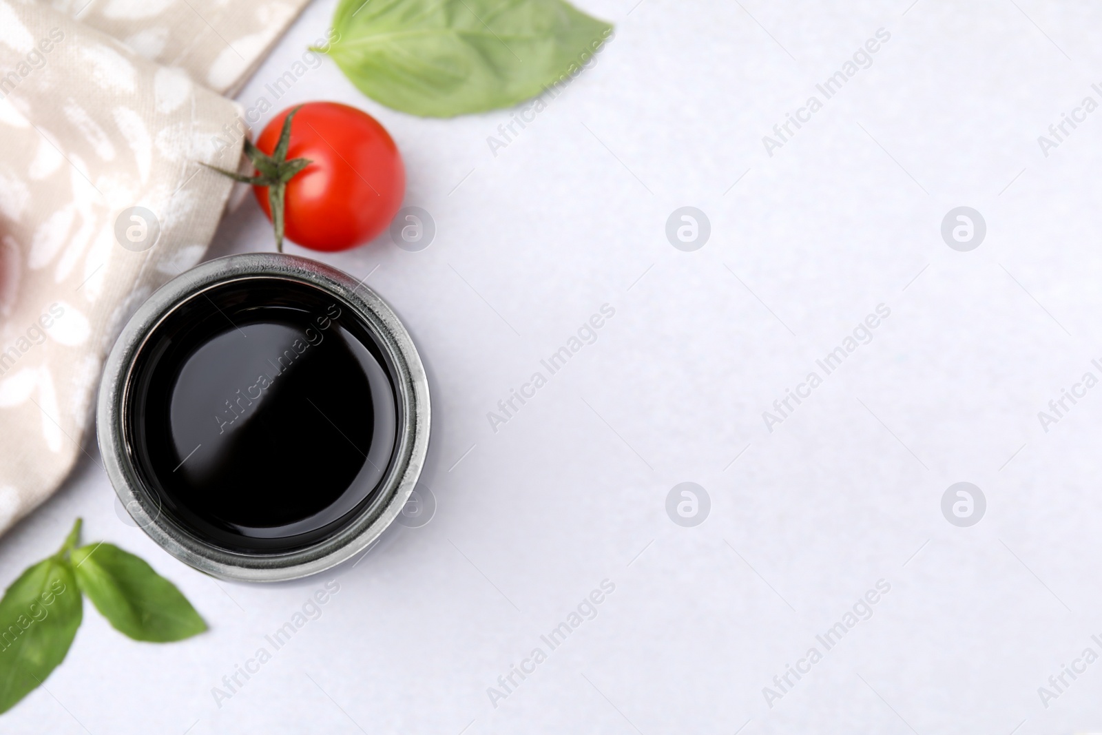 Photo of Balsamic vinegar, basil and tomato on white table, flat lay. Space for text