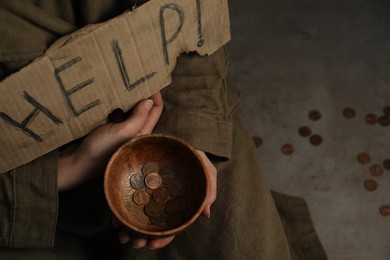 Poor homeless woman with help sign holding bowl of donations on floor, closeup. Space for text