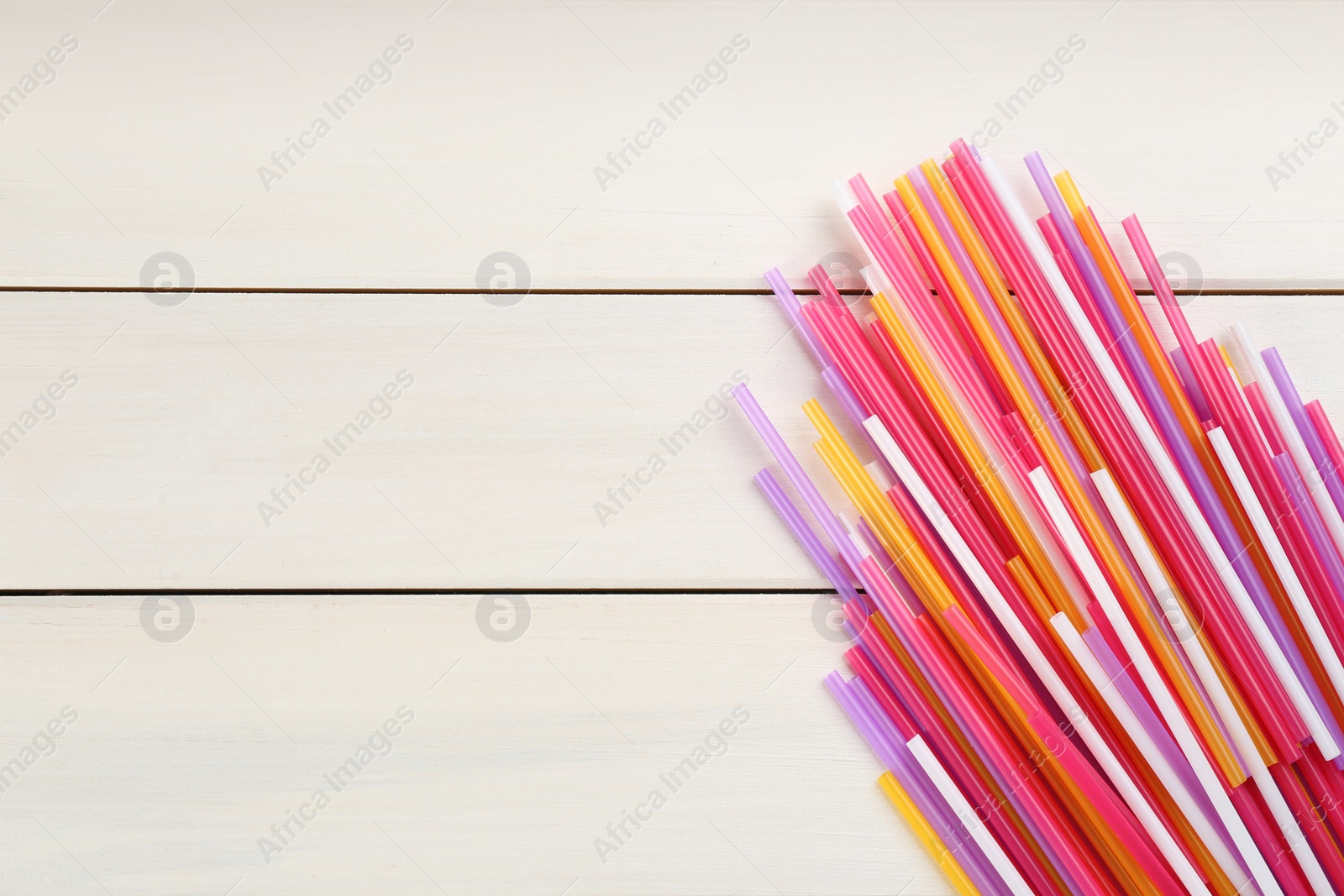 Photo of Colorful plastic drinking straws on white wooden table, flat lay. Space for text