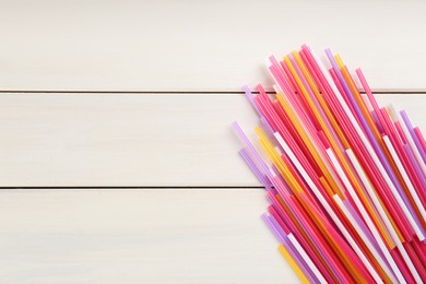 Colorful plastic drinking straws on white wooden table, flat lay. Space for text