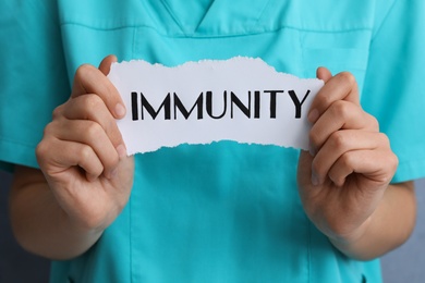Photo of Woman holding paper piece with word Immunity, closeup
