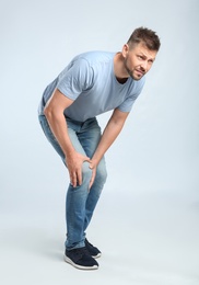 Full length portrait of man having knee problems on grey background