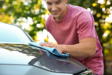 Young man washing car hood with rag outdoors