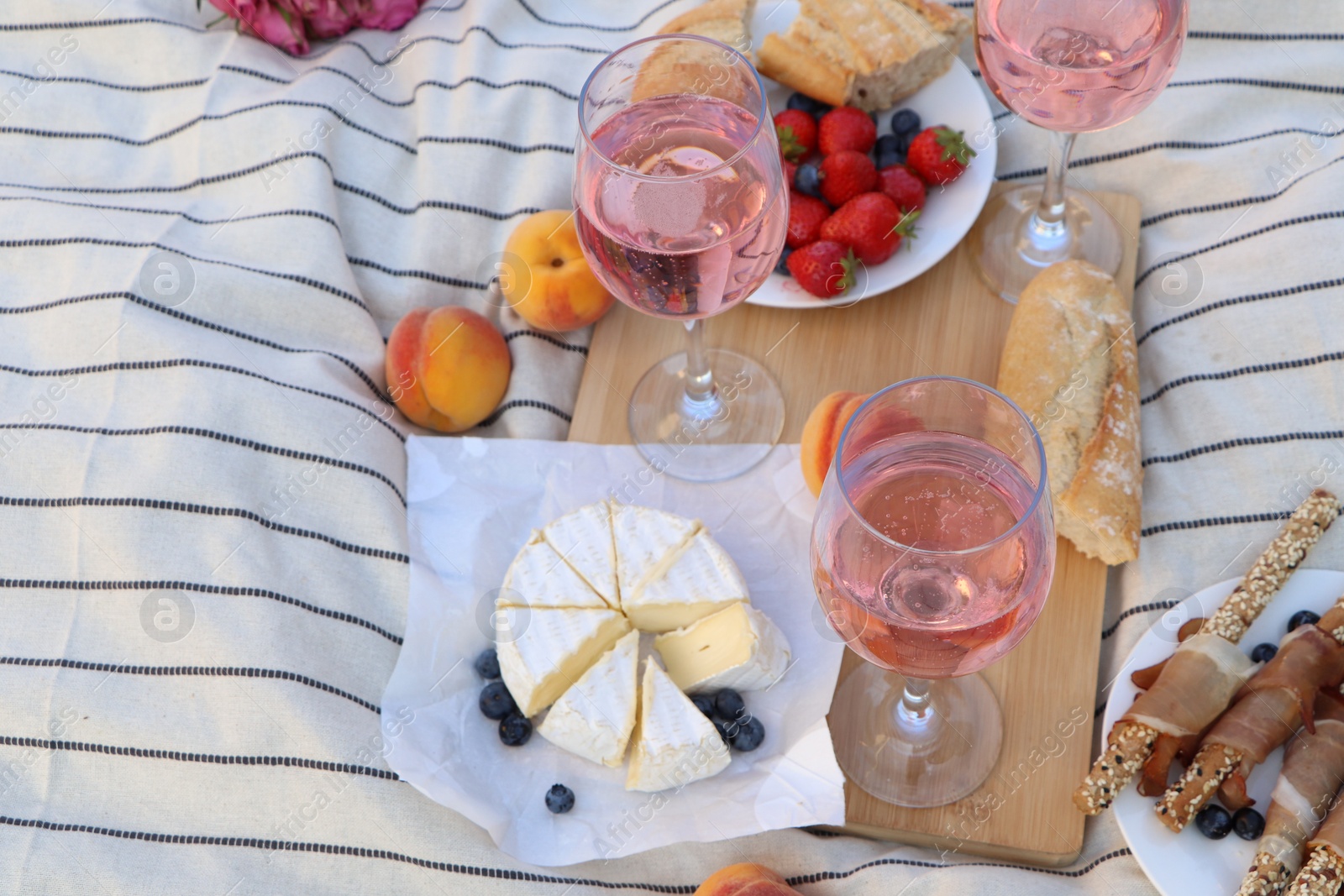 Photo of Glasses of delicious rose wine and food on white picnic blanket