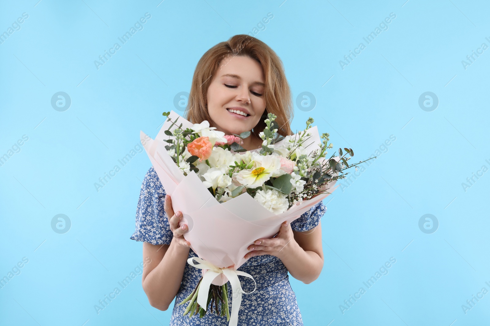 Photo of Happy woman with bouquet of beautiful flowers on light blue background