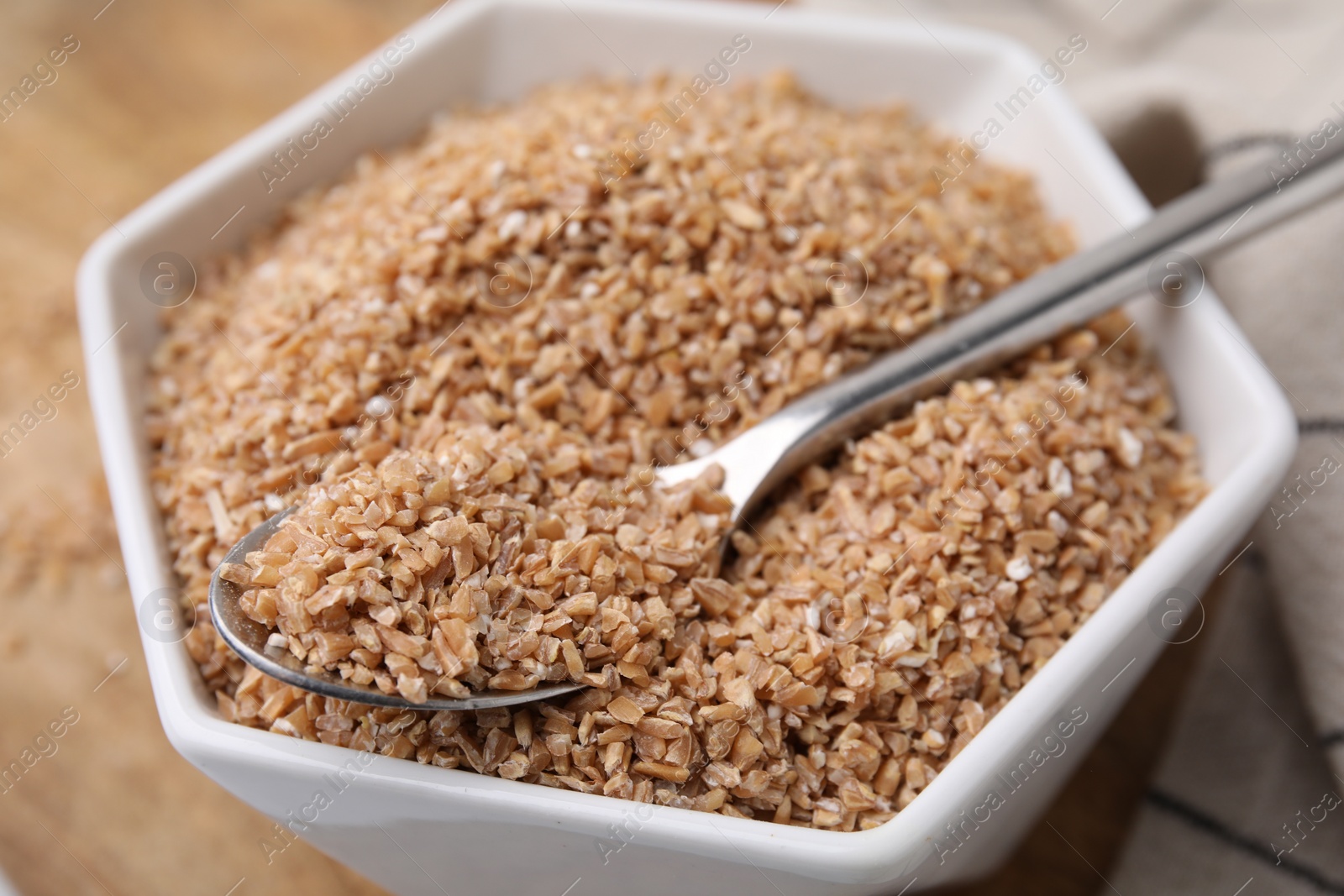 Photo of Dry wheat groats and spoon in bowl on table, closeup