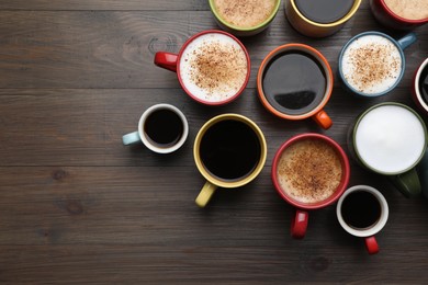 Photo of Many different cups with aromatic hot coffee on wooden table, flat lay. Space for text