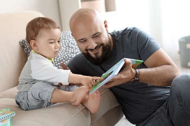 Photo of Dad reading book with his little son in living room