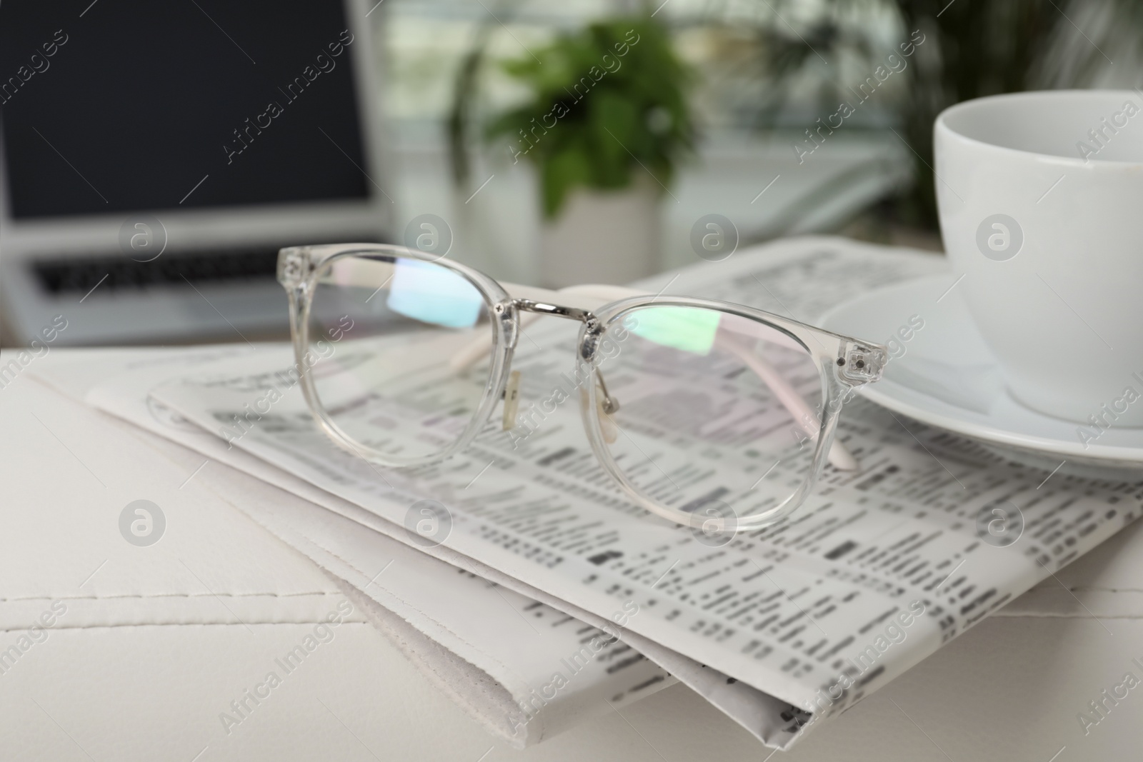 Photo of Newspapers, glasses and cup of drink on armrest indoors