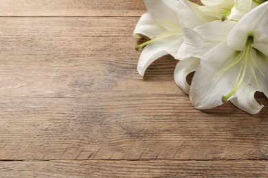 Photo of Beautiful white lily flowers on wooden table, space for text