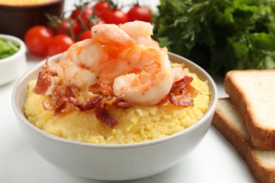 Photo of Fresh tasty shrimps, bacon and grits in bowl on white table, closeup