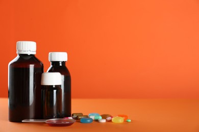 Bottles of cough syrup, dosing spoon and pills on orange background. Space for text