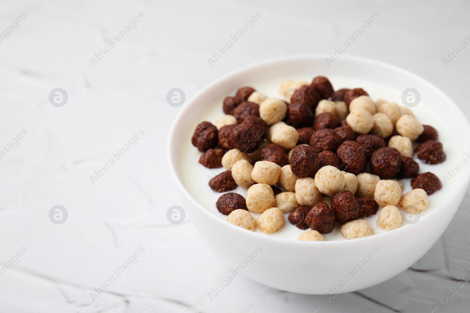 Photo of Breakfast cereal. Tasty corn balls with milk in bowl on white textured table, closeup. Space for text