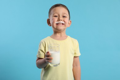 Photo of Cute boy with milk mustache holding glass of tasty dairy drink on light blue background