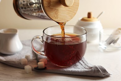 Photo of Pouring warm tea into cup on white wooden table, closeup