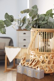 Wicker basket with beautiful eucalyptus branches and phrase Hello Baby on wooden table indoors. Interior design