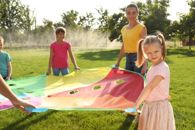 Photo of Group of children and teacher playing with rainbow playground parachute on green grass. Summer camp activity