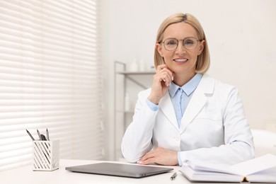 Portrait of happy dermatologist at white table in clinic