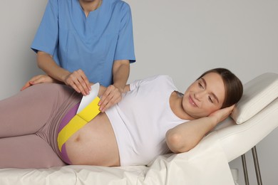 Photo of Pregnant woman visiting physiotherapist. Doctor applying kinesio tape indoors, closeup