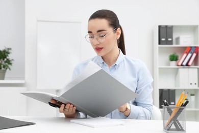 Photo of Young female intern with folder working at table in office