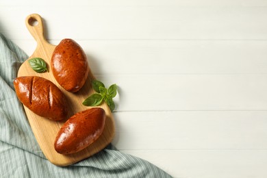 Photo of Delicious baked pirozhki and basil on white wooden table, top view. Space for text