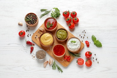 Flat lay composition with different sauces and ingredients on white wooden background