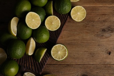 Photo of Fresh whole and cut limes on wooden table, flat lay. Space for text