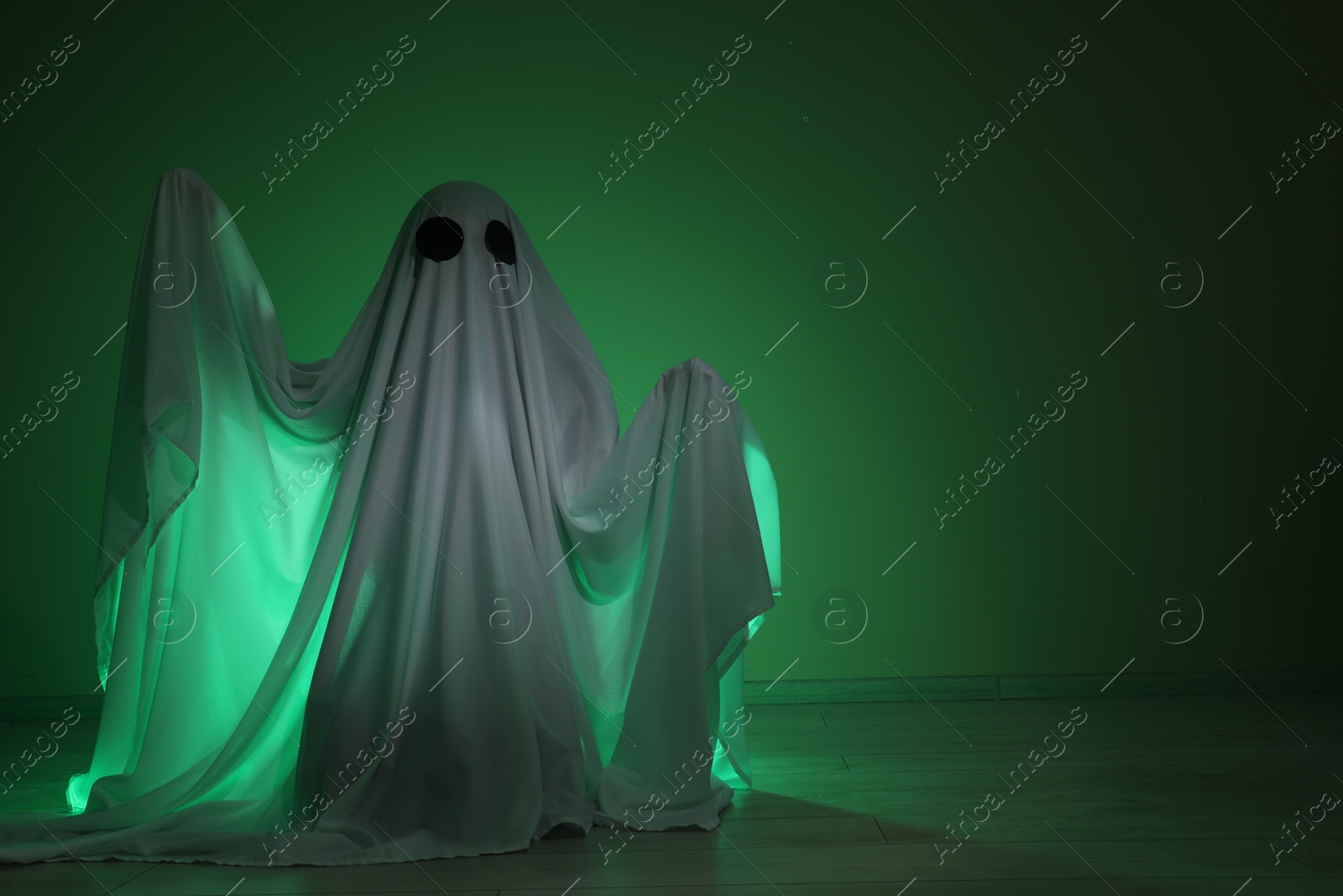 Photo of Creepy ghost. Woman covered with sheet in green light, space for text