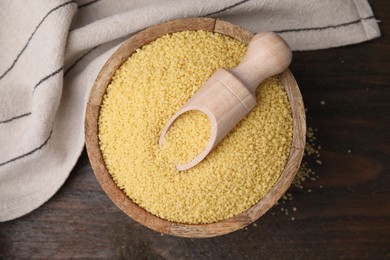 Bowl and scoop with raw couscous on wooden table, top view