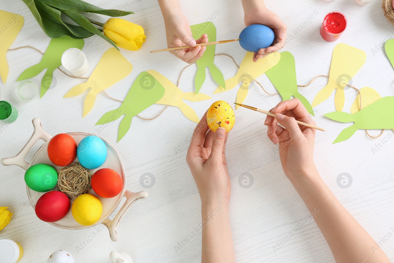 Photo of Mother and her child painting Easter eggs at table, top view