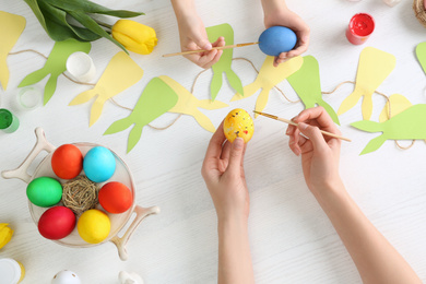 Photo of Mother and her child painting Easter eggs at table, top view