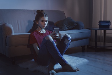 Photo of Upset teenage girl with smartphone in dark room. Danger of internet