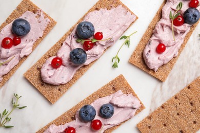 Photo of Tasty cracker sandwiches with cream cheese, blueberries, red currants and thyme on white marble board, flat lay