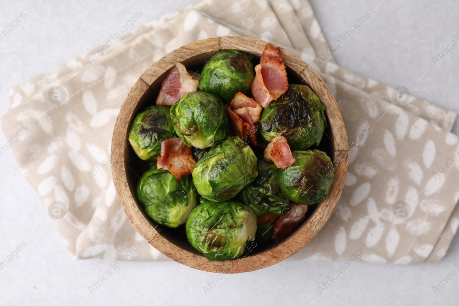 Photo of Delicious roasted Brussels sprouts and bacon in bowl on light table, top view