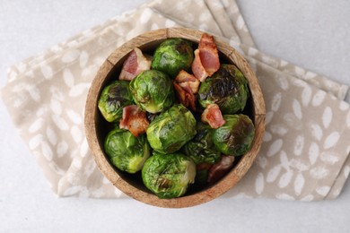 Delicious roasted Brussels sprouts and bacon in bowl on light table, top view