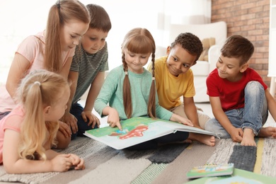 Photo of Cute little children reading book together indoors. Learning by playing