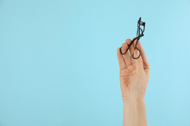 Photo of Woman holding eyelash curler on light blue background, closeup. Space for text