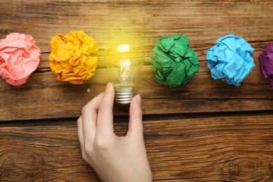 Photo of Woman holding lightbulb among colorful paper balls at wooden table, top view. Idea concept