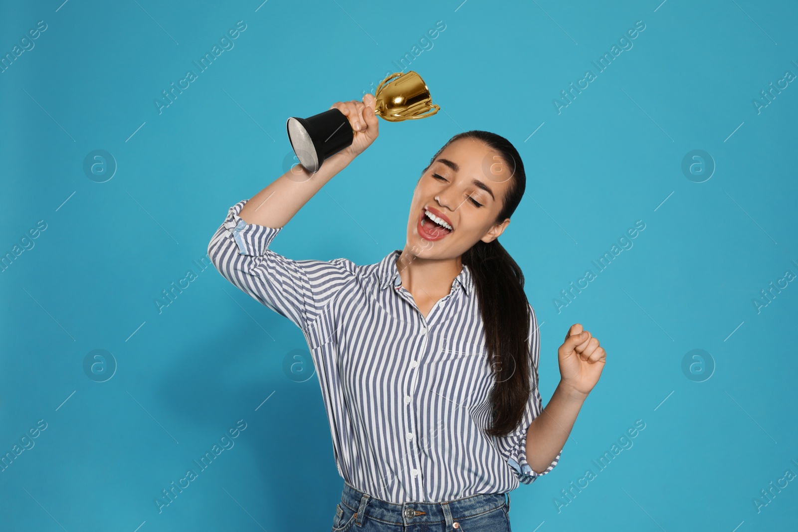 Photo of Portrait of happy young woman with gold trophy cup on blue background