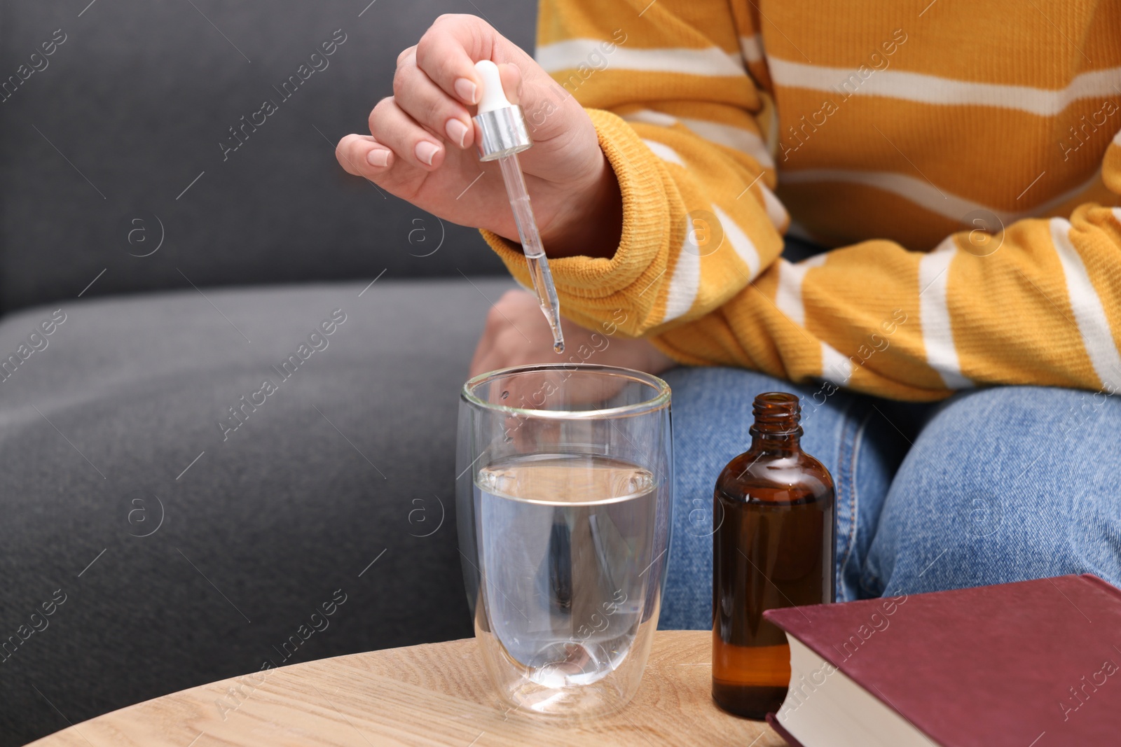 Photo of Woman dripping food supplement into glass of water on wooden table indoors, closeup. Space for text