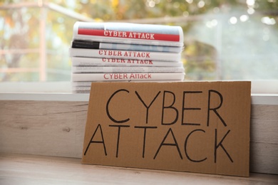 Photo of Cardboard with words CYBER ATTACK and newspapers on window sill, closeup