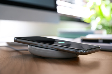 Photo of Smartphone charging with wireless pad on desk. Modern workplace