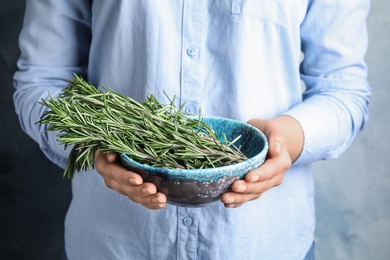 Young woman holding bowl of fresh rosemary, closeup